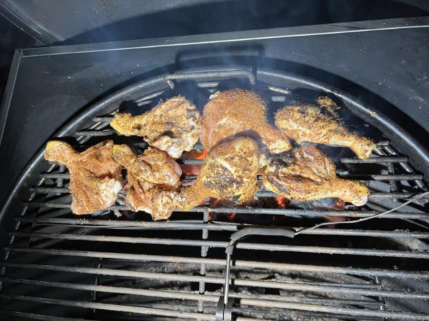 Butterflied chicken legs cooking over the coals on a Weber kettle grill.