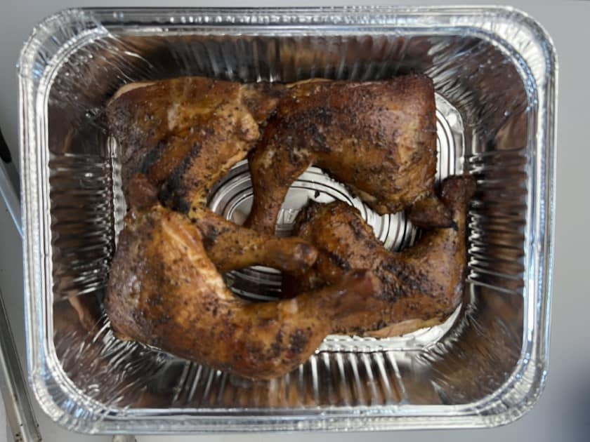 Weber kettle smoked chicken quarters resting in a foil pan.