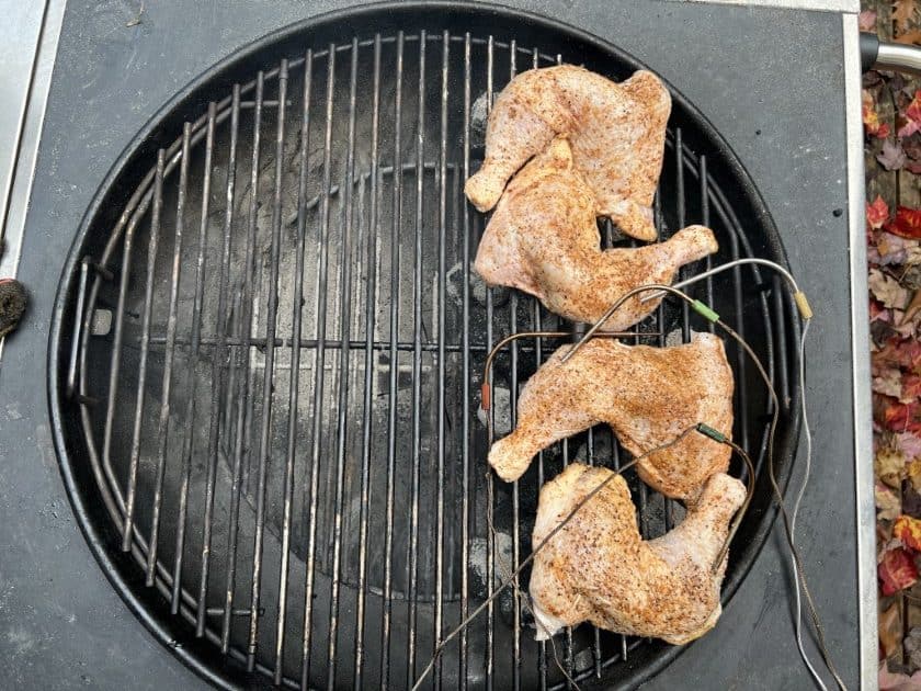 Four chicken quarters directly over the coals on a Weber kettle grill.