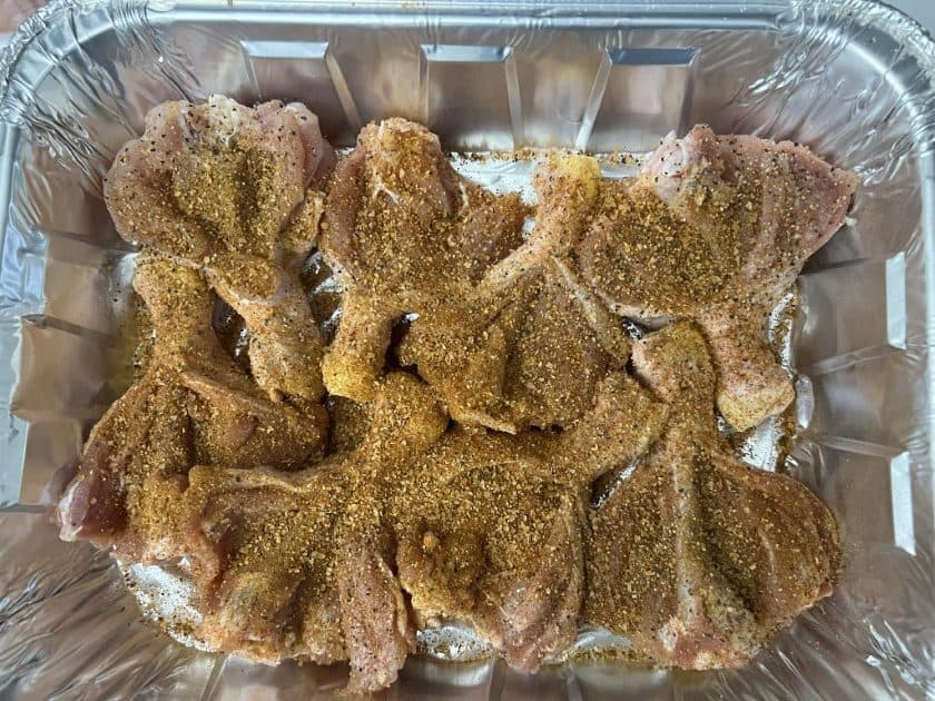 Butterflied chicken legs in a foil pan dry brining in spices.