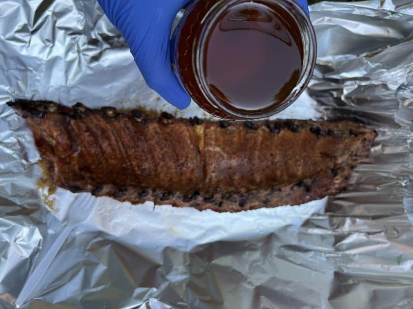 Pouring honey on ribs as they are being wrapped in aluminum foil.