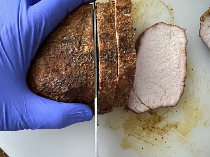Slicing the BBQ pork loin on a white cutting board.