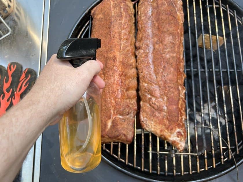 Spritzing ribs with apple juice and apple cider vinegar.